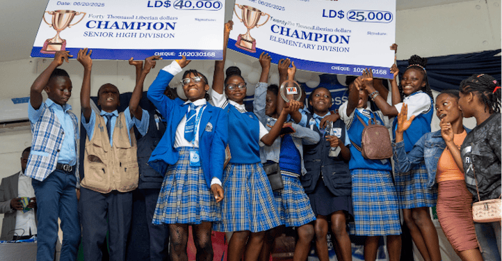 Students from Kings and Queens International School celebrate winning first place in the YMA National Press Club Exhibition, holding L$25,000 and L$40,000 championship checks on stage