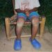 A young boy sits with hands clasped and legs bruised, representing child trauma and neglect in rural Bong County, Liberia