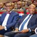 Liberian President Joseph Nyuma Boakai and African Development Bank President Dr. Akinwumi Adesina sit side by side at a high-level government event in Monrovia, surrounded by officials and dignitaries, with red, white, and blue decorations symbolizing national pride.
