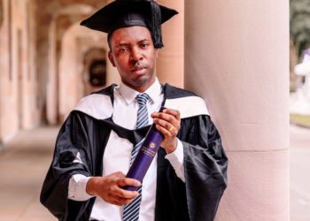 Alfred H. W. Brownell Jr. standing in a library aisle, wearing a checkered shirt, preparing for his graduation from the TC Beirne School of Law.