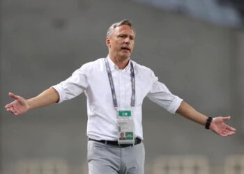 Antoine Hey gestures on the touchline during a match, wearing a white shirt and lanyard, as he takes charge of Algerian club ES Sétif.