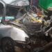 Damaged silver vehicle mangled in a fatal crash with a Bea Mountain supply truck on the Ibrahim Banbagada Highway, as bystanders gather and police investigate.