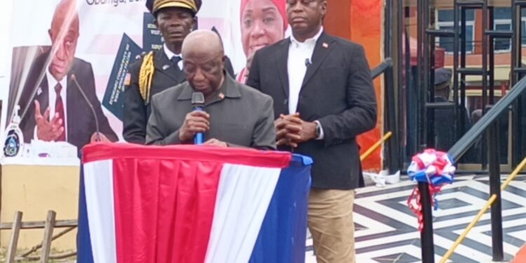 President Joseph Boakai speaks at the launch of Liberia’s first regional passport center in Gbarnga, Bong County, flanked by security personnel and officials under red, white, and blue decorations
