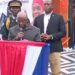 President Joseph Boakai speaks at the launch of Liberia’s first regional passport center in Gbarnga, Bong County, flanked by security personnel and officials under red, white, and blue decorations
