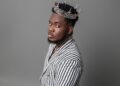 Liberian artist CIC wears a silver crown and a striped suit, embodying his “Local Champion” persona in a powerful promotional portrait for his 2025 album release.