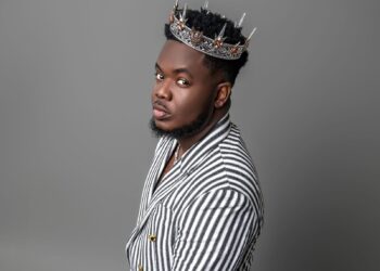 Liberian artist CIC wears a silver crown and a striped suit, embodying his “Local Champion” persona in a powerful promotional portrait for his 2025 album release.