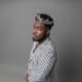 Liberian artist CIC wears a silver crown and a striped suit, embodying his “Local Champion” persona in a powerful promotional portrait for his 2025 album release.