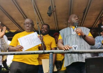 Representative Marvin Cole holds up CMC party document as Musa Bility looks on during a political rally in Bong County.