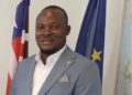 Township Commissioner Edward Horton Lahai stands near national and EU flags, highlighting governance challenges faced by local officials across Liberia.