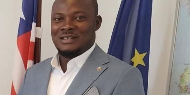 Township Commissioner Edward Horton Lahai stands near national and EU flags, highlighting governance challenges faced by local officials across Liberia.