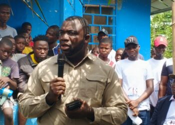 Rep. James Kolleh speaks into a microphone during a public gathering at Radio Gbartala's 13th anniversary celebration, surrounded by community members and supporters in Bong County, Liberia.