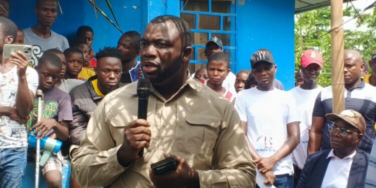 Rep. James Kolleh speaks into a microphone during a public gathering at Radio Gbartala's 13th anniversary celebration, surrounded by community members and supporters in Bong County, Liberia.