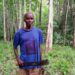 Liberian farmer Joseph Dumoe stands with cutlass in his Suakoko District farmland, wearing a political campaign shirt