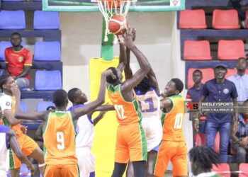 Liberia U16 basketball players in orange and green contest a rebound under the hoop against Benin during an intense FIBA Africa Zone 3 qualifier at SKD Gymnasium in Paynesville.
