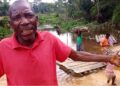 Frustrated elder in Loguatuo, Nimba County, pleads for bridge construction over the deadly Louhn River as residents cross on a makeshift raft in the background