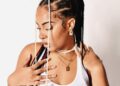 Liberian socialite Michelle Doe poses in a white tank top with intricately braided hair adorned with beads and pearls, symbolizing her strength and individuality as highlighted in her public journey of resilience and reinvention