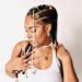 Liberian socialite Michelle Doe poses in a white tank top with intricately braided hair adorned with beads and pearls, symbolizing her strength and individuality as highlighted in her public journey of resilience and reinvention