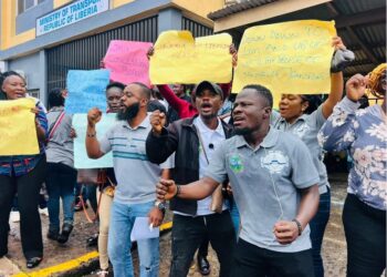 Citizens protest in front of the Ministry of Transport in Monrovia, holding placards demanding faster passport processing and license issuance.