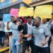 Citizens protest in front of the Ministry of Transport in Monrovia, holding placards demanding faster passport processing and license issuance.