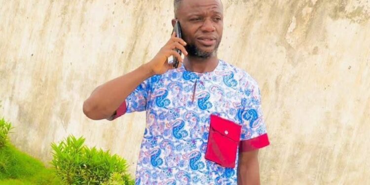Julius Sevelee, the teacher suspended in Bong County, stands on his phone near a school compound.