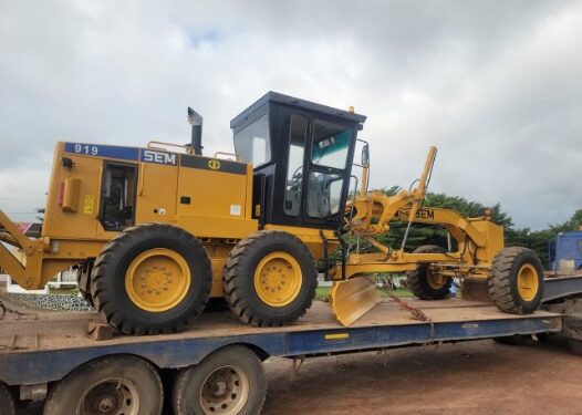 Caterpillar motor grader loaded on trailer for transport to road construction site in Liberia