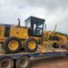 Caterpillar motor grader loaded on trailer for transport to road construction site in Liberia