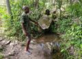 Bong County resident pointing to a shallow bush water source still used for drinking in Laykai-Ta village
