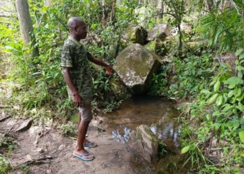 Bong County resident pointing to a shallow bush water source still used for drinking in Laykai-Ta village