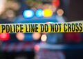 Shallow depth of field image taken of yellow law enforcement line with police car and lights in the background.