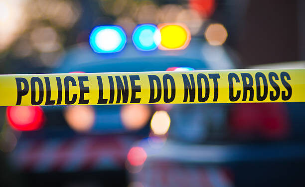 Shallow depth of field image taken of yellow law enforcement line with police car and lights in the background.