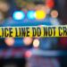 Shallow depth of field image taken of yellow law enforcement line with police car and lights in the background.