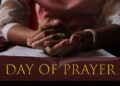 Close-up of a person's clasped hands resting on an open Bible, symbolizing prayer and reflection, with the words "Day of Prayer" in gold text across the bottom of the image.