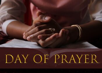 Close-up of a person's clasped hands resting on an open Bible, symbolizing prayer and reflection, with the words "Day of Prayer" in gold text across the bottom of the image.