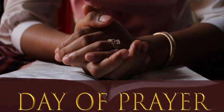 Close-up of a person's clasped hands resting on an open Bible, symbolizing prayer and reflection, with the words "Day of Prayer" in gold text across the bottom of the image.