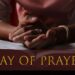 Close-up of a person's clasped hands resting on an open Bible, symbolizing prayer and reflection, with the words "Day of Prayer" in gold text across the bottom of the image.