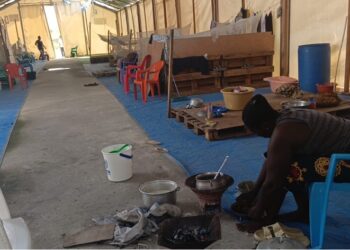 Liberian returnee woman prepares food inside deteriorating shelter at CARI compound in Suakoko, Bong County