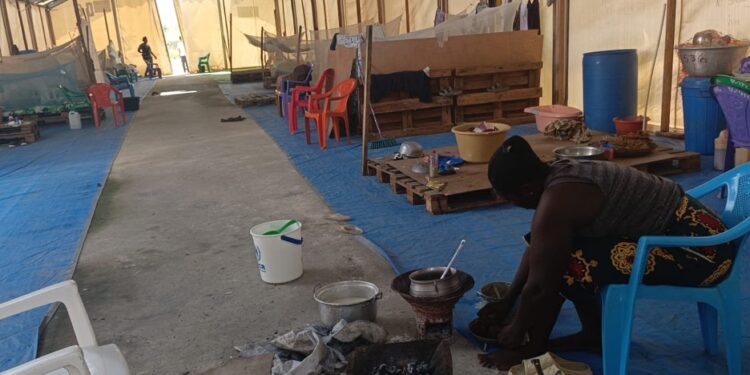 Liberian returnee woman prepares food inside deteriorating shelter at CARI compound in Suakoko, Bong County