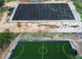 Before-and-after aerial views of a FIFA-funded mini-football pitch site in Liberia under the Arena Project, showing transformation from soil base to synthetic turf.