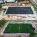 Before-and-after aerial views of a FIFA-funded mini-football pitch site in Liberia under the Arena Project, showing transformation from soil base to synthetic turf.