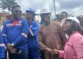 Representative Jeremiah Sokan Sr. in a brown kaftan greets a female engineer during a site visit in Grand Gedeh County, surrounded by local workers and project staff.
