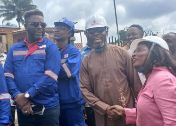 Representative Jeremiah Sokan Sr. in a brown kaftan greets a female engineer during a site visit in Grand Gedeh County, surrounded by local workers and project staff.