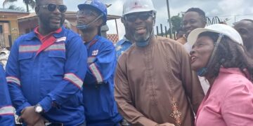 Representative Jeremiah Sokan Sr. in a brown kaftan greets a female engineer during a site visit in Grand Gedeh County, surrounded by local workers and project staff.