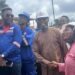 Representative Jeremiah Sokan Sr. in a brown kaftan greets a female engineer during a site visit in Grand Gedeh County, surrounded by local workers and project staff.