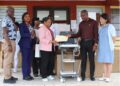 Dr. Teyah S. Moore hands over documents for new ultrasound machines to JFK CEO Dr. Linda Birch, with Ministry of Health and hospital staff present.