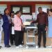 Dr. Teyah S. Moore hands over documents for new ultrasound machines to JFK CEO Dr. Linda Birch, with Ministry of Health and hospital staff present.