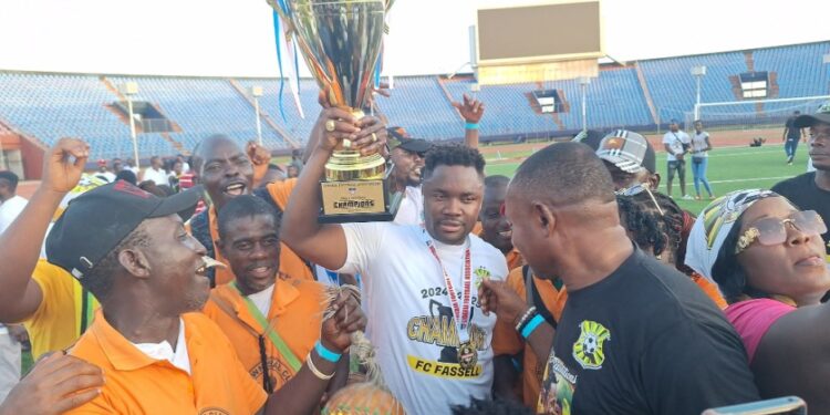 FC Fassell CEO and LFA presidential hopeful Cassell Kuoh celebrating with a trophy surrounded by supporters at a football stadium