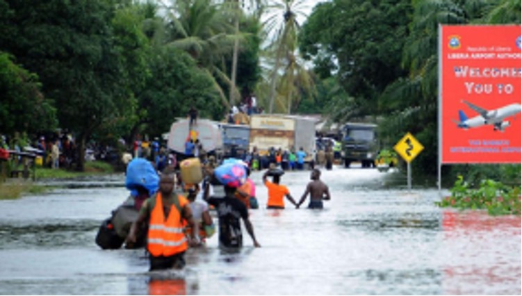 Flooded road near Liberia’s international airport, with residents wading through water—highlighting climate-induced disasters.