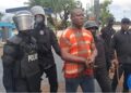 Liberian police escort ex-West Point Commissioner in handcuffs during CDC compound raid in Monrovia.