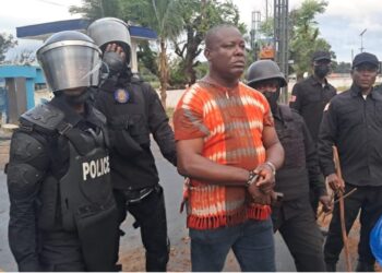 Liberian police escort ex-West Point Commissioner in handcuffs during CDC compound raid in Monrovia.