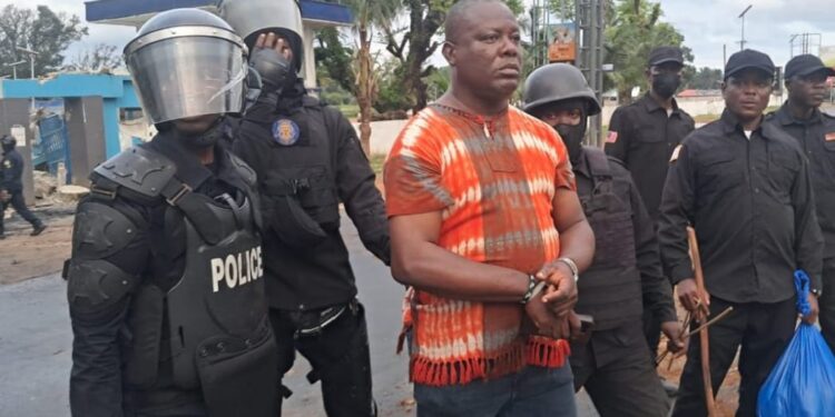Liberian police escort ex-West Point Commissioner in handcuffs during CDC compound raid in Monrovia.